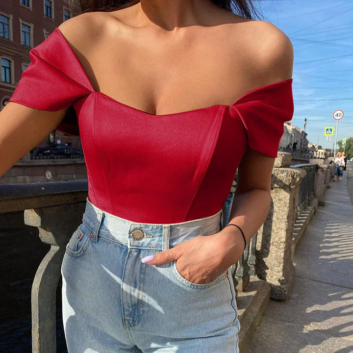 Woman wearing a red off-shoulder top and high-waisted light blue jeans standing by a stone railing outdoors