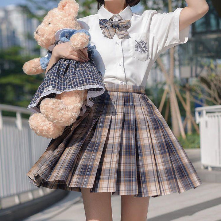 Young woman in white shirt and plaid skirt holding teddy bear dressed in blue plaid outfit outdoors