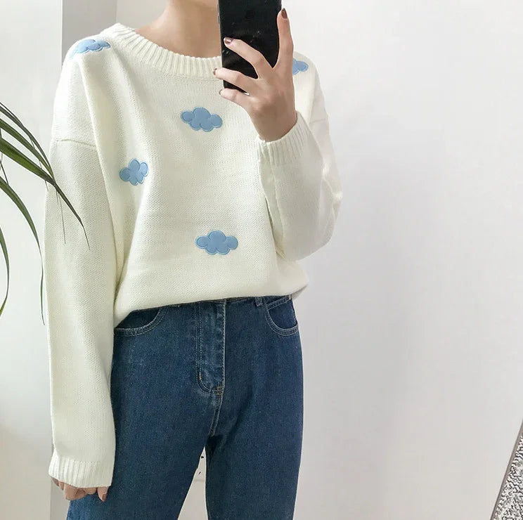 Person wearing white sweater with blue cloud prints and blue jeans taking mirror selfie