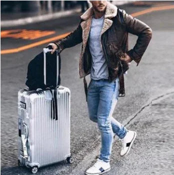 Man in brown shearling jacket and jeans walking with silver hard-shell suitcase on street