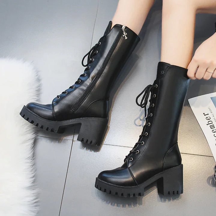 Black leather mid-calf lace-up boots with chunky heels and side zippers on gray tiled floor