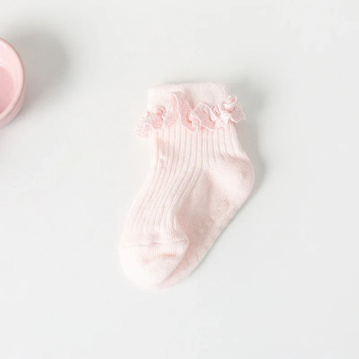 Soft pink baby sock with ruffled lace trim, ribbed texture, on white background