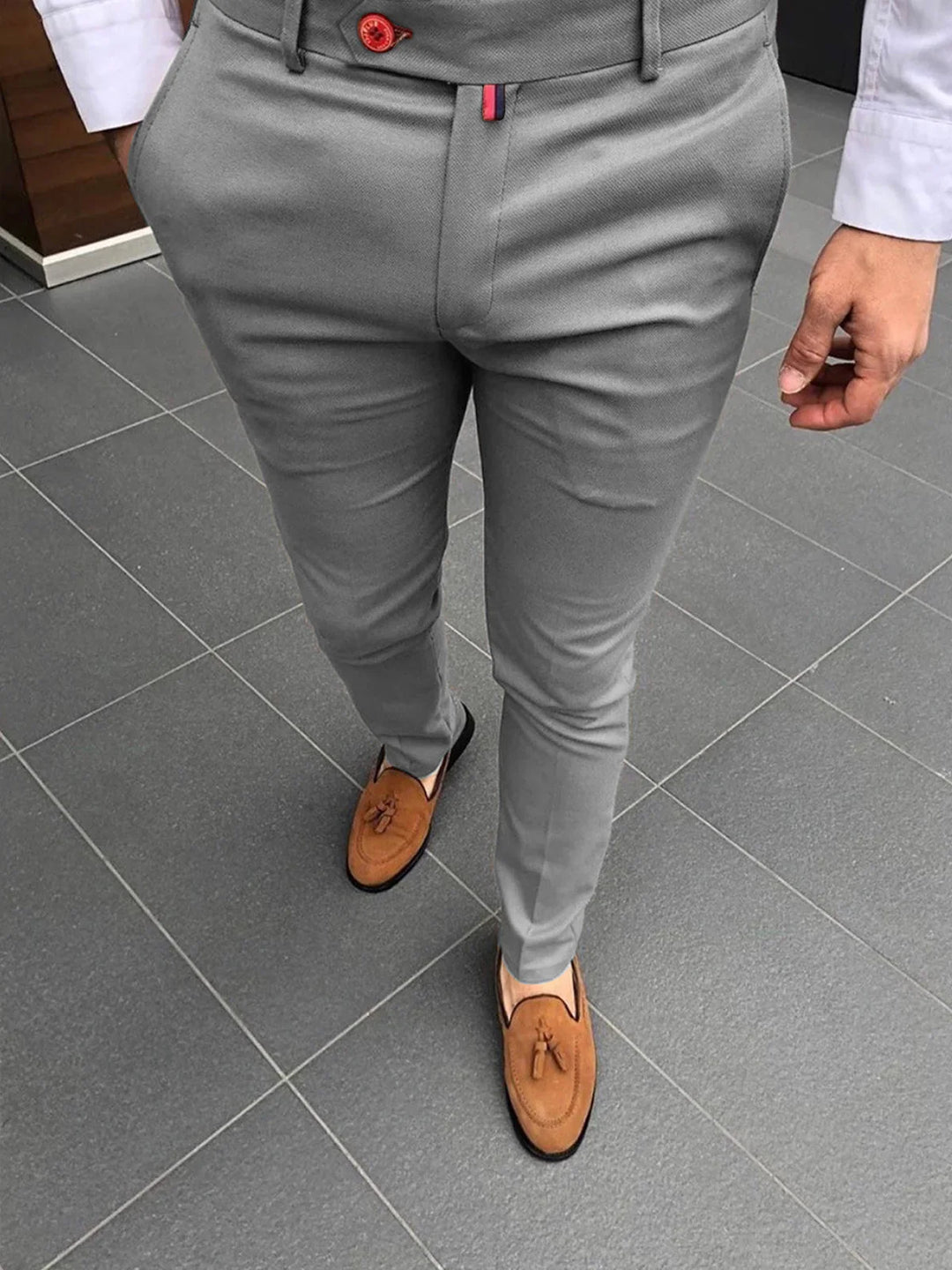 Man wearing grey slim-fit pants with red button and brown tassel loafers on tiled floor