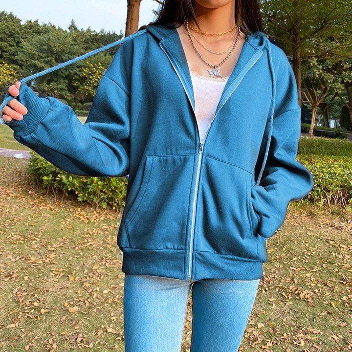 Woman wearing blue zip-up hoodie and light blue jeans outdoors in autumn park