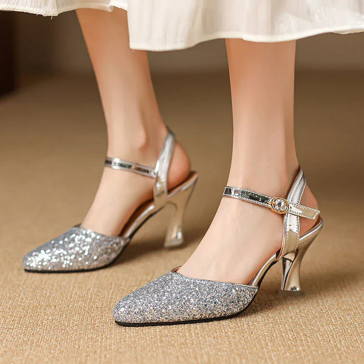 Silver glitter pointed toe high heel sandals with ankle straps and gold buckles on beige carpet