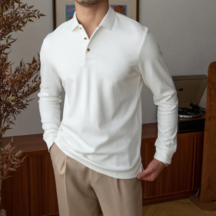 Man wearing white long-sleeve polo shirt and beige trousers in stylish indoor setting