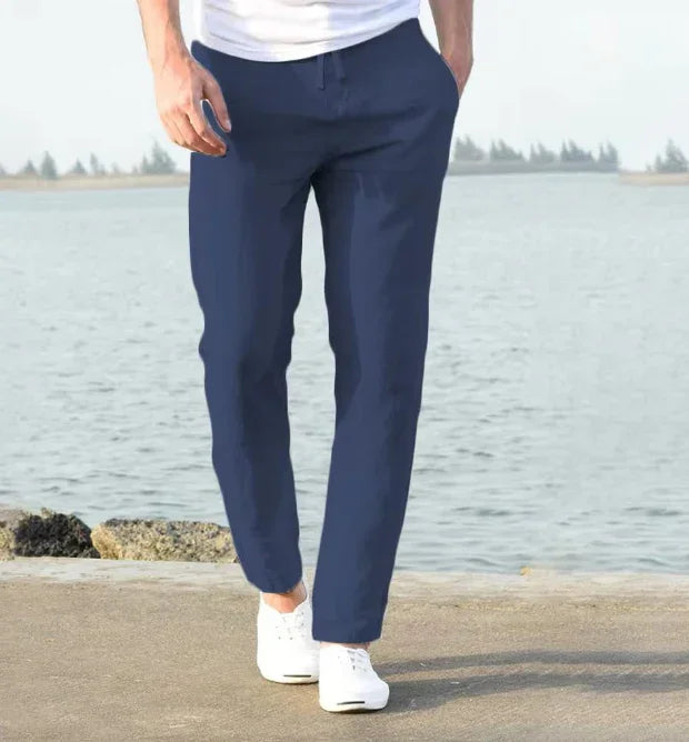 Man wearing navy blue casual pants and white sneakers walking by a lakeside on a sunny day
