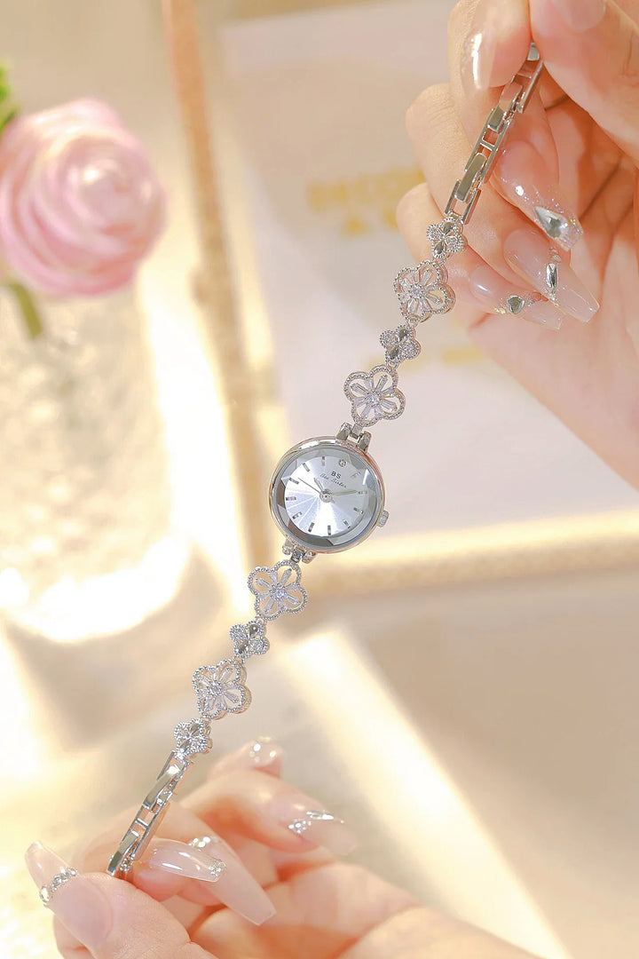 Elegant silver floral bracelet watch held by hands with clear, decorated nails