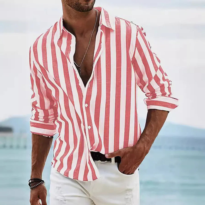 Man wearing casual red and white vertical striped shirt with rolled sleeves and white pants by the beach