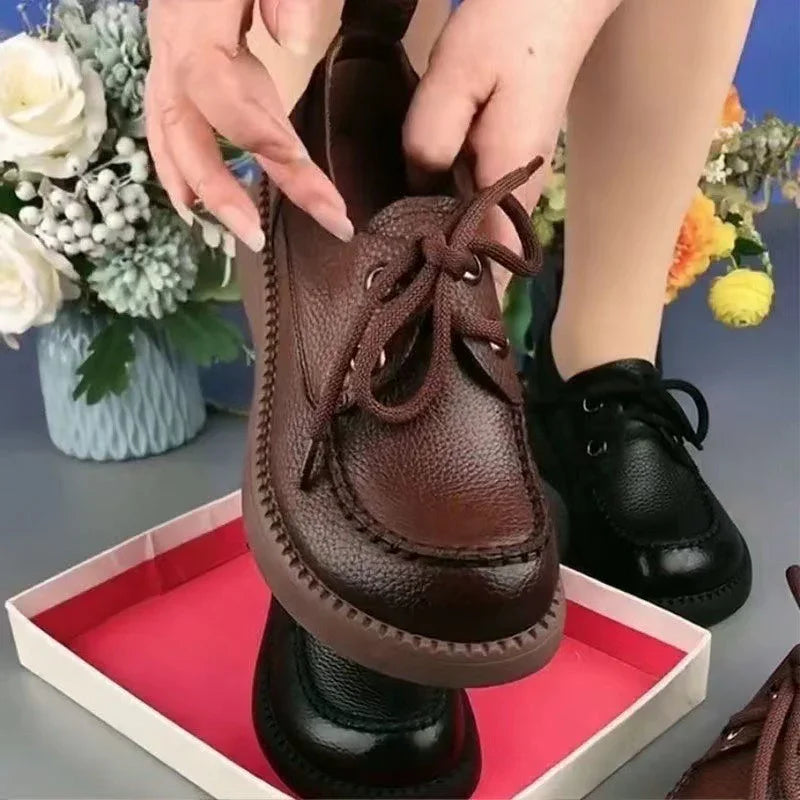 Hands holding brown leather lace-up casual shoes with black shoes worn on feet in background