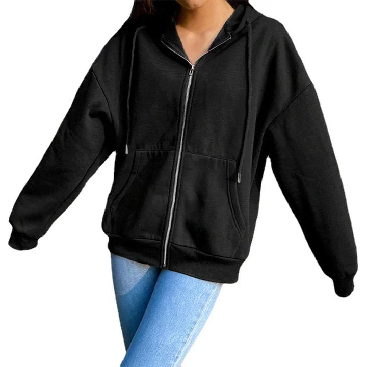 Woman wearing black zip-up hoodie with front pockets and hood, paired with light blue jeans