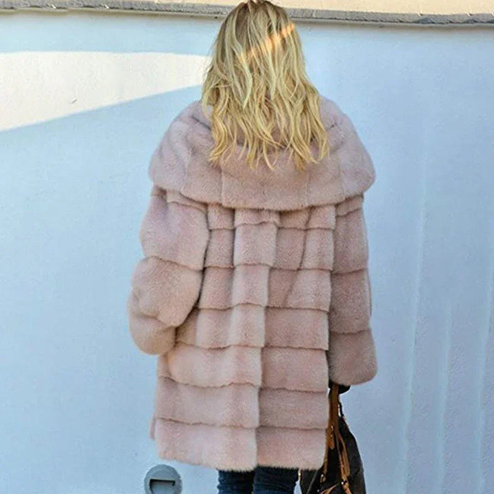 Rear view of woman wearing a plush pink fur coat and holding a black handbag against a white wall