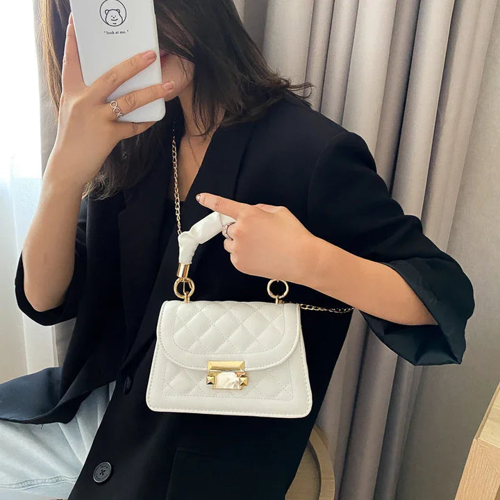 Woman in black blazer holding a white quilted handbag with gold chain and clasp