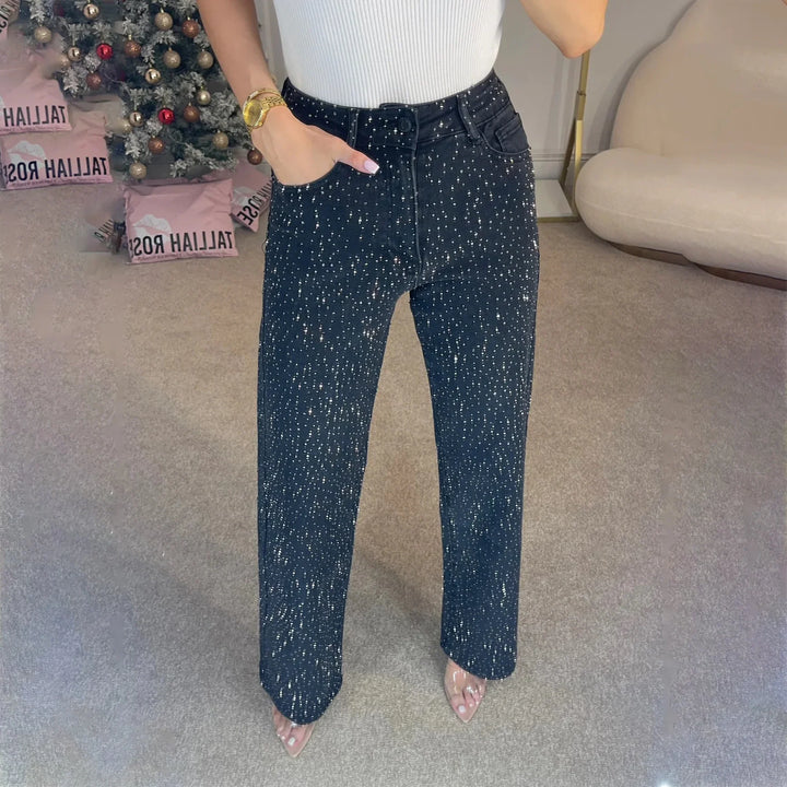 Woman wearing high-waisted black jeans with silver sparkles and a white ribbed top indoors