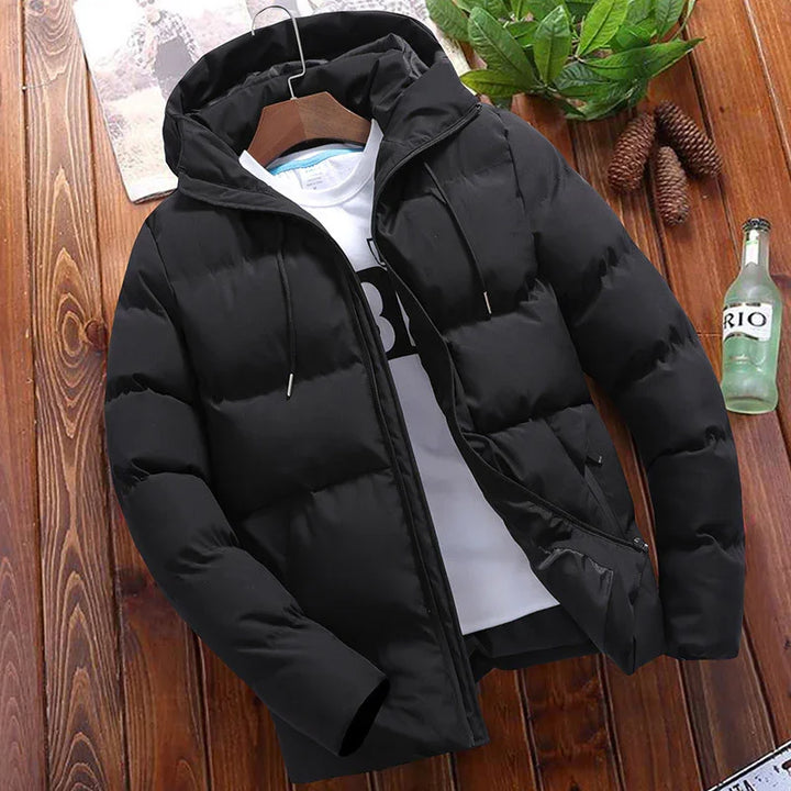 Black puffer jacket with hood on wooden surface, white graphic t-shirt inside, green leaves and glass bottle nearby