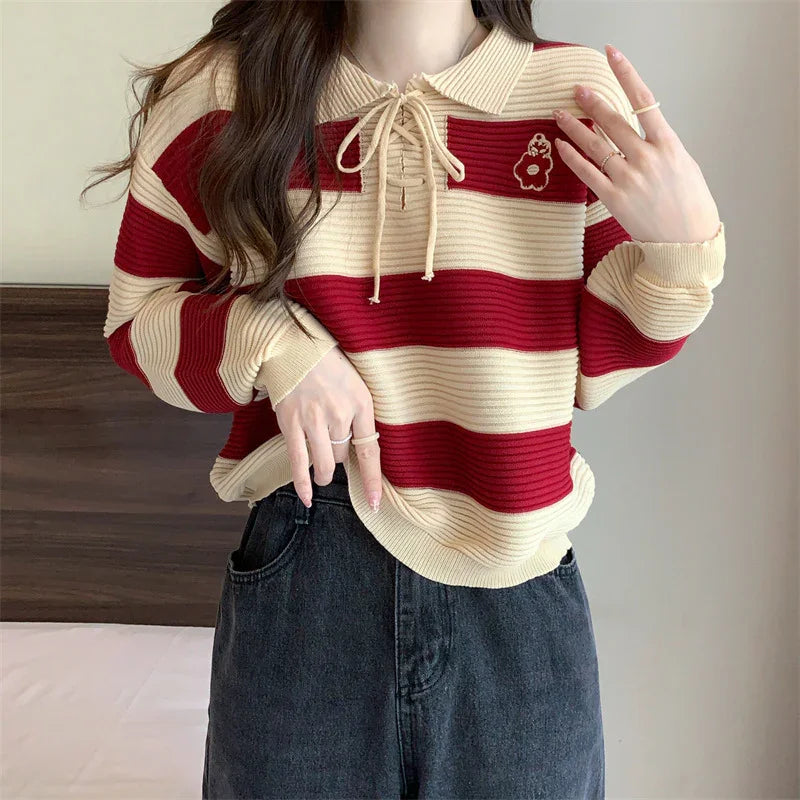 Woman wearing red and beige striped knit sweater with collar and bow, paired with black denim jeans