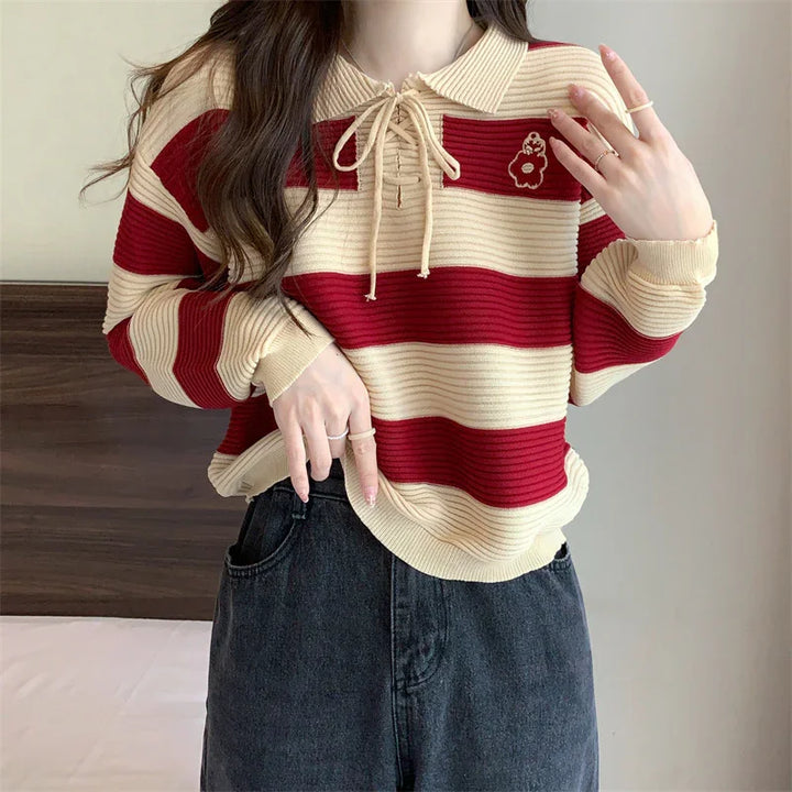 Woman wearing red and beige striped knit sweater with collar and bow, paired with black denim jeans