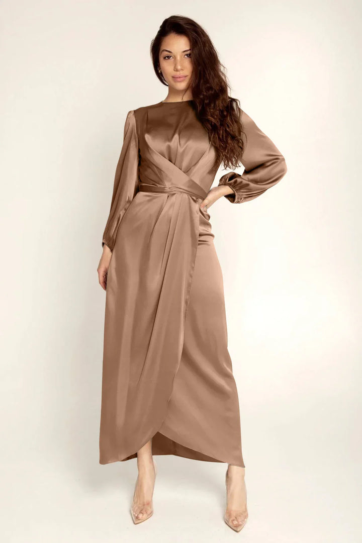 Woman wearing a long brown satin dress with puff sleeves and wrap detail, posing on white background