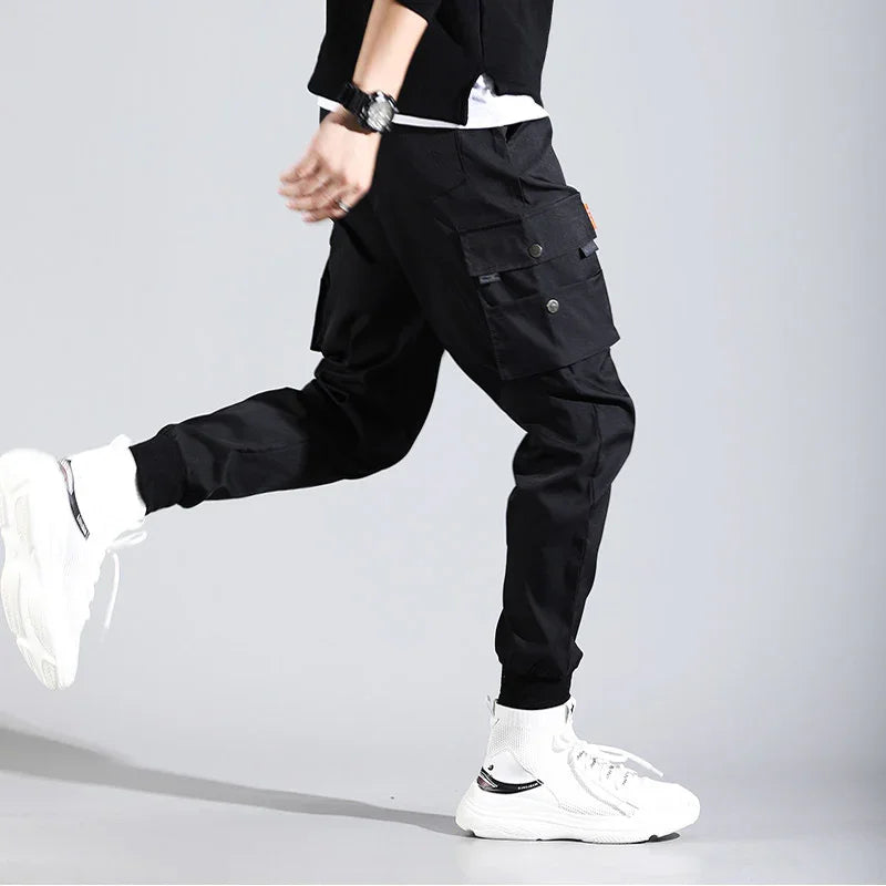Person wearing black cargo pants with buttoned pockets and white sneakers against gray background