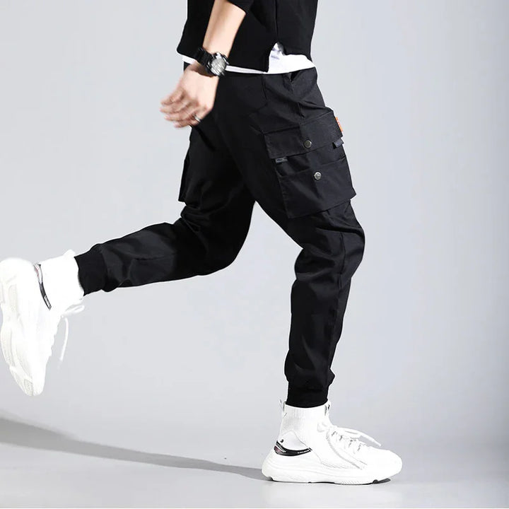 Person wearing black cargo pants with buttoned pockets and white sneakers against gray background