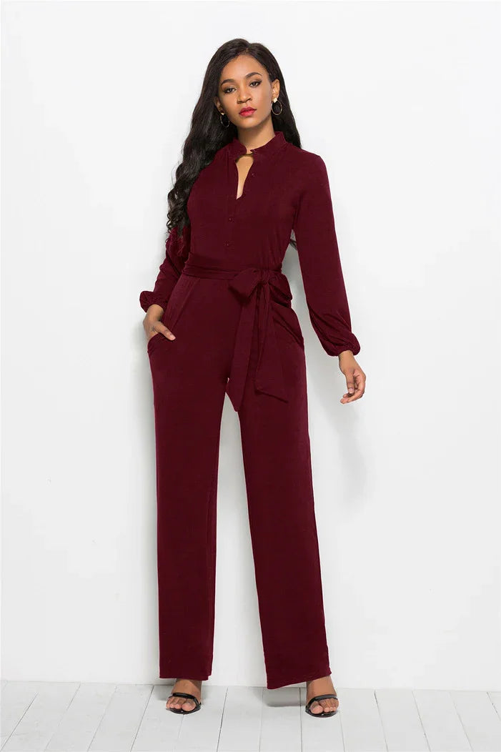 Elegant woman wearing a burgundy long-sleeve jumpsuit with a waist tie and black heeled sandals