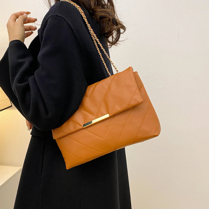 Woman wearing black coat holding a tan quilted leather handbag with gold chain strap