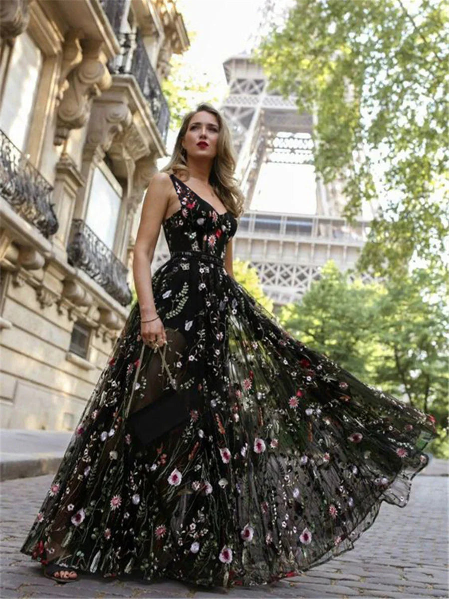 Woman in long black floral embroidered dress posing near Eiffel Tower in Paris street