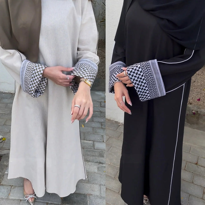 Two women wearing stylish abayas in beige and black with patterned sleeve cuffs and white piping