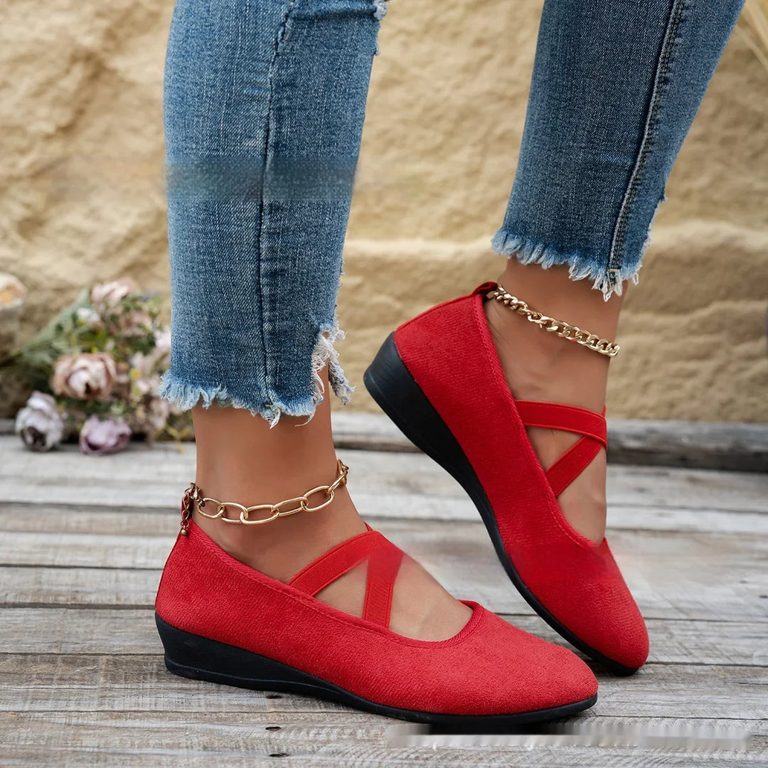 Red wedge shoes with crisscross straps worn with distressed blue jeans and gold anklets on wooden floor
