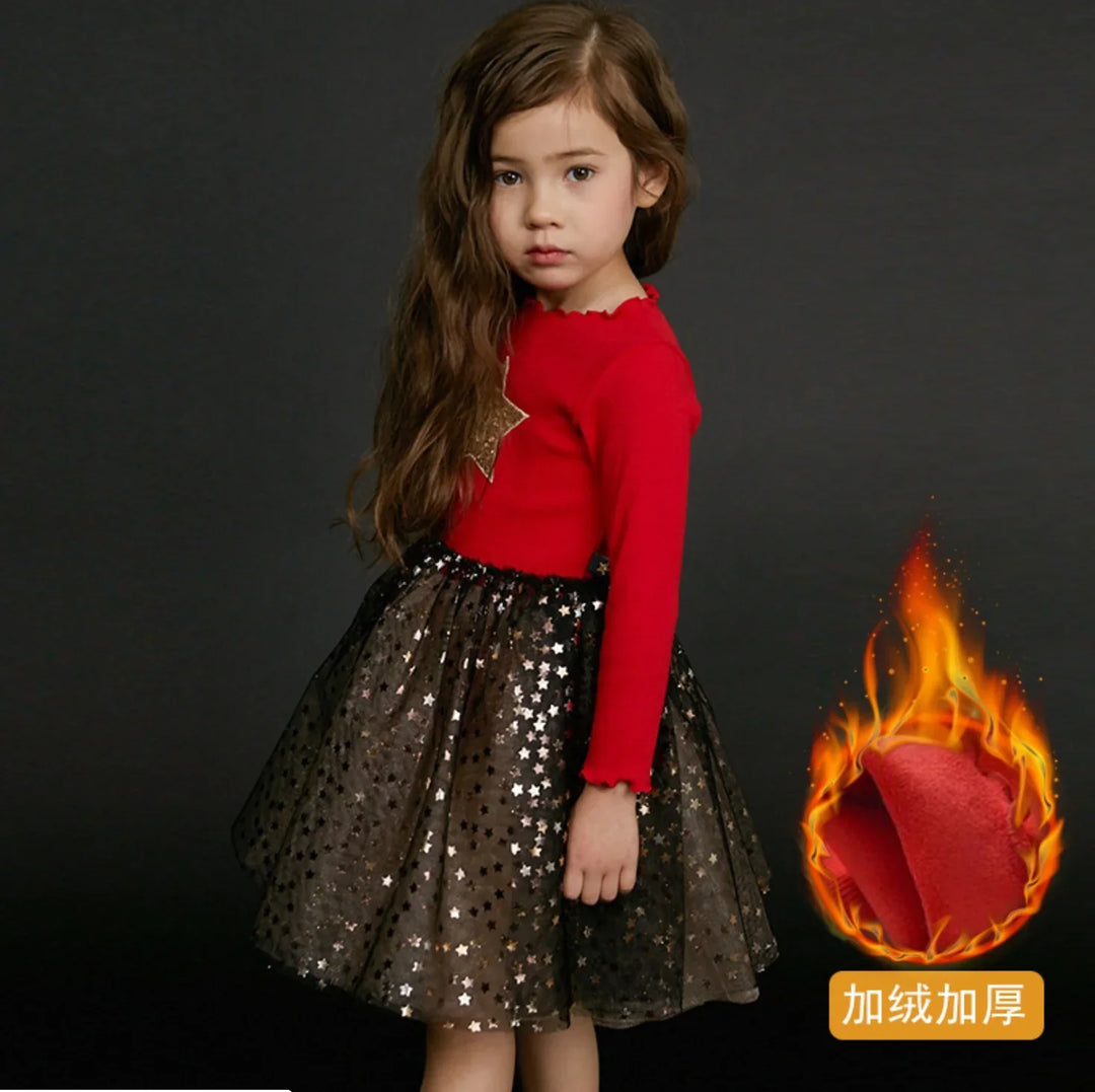 Young girl wearing red long-sleeve top with gold star and black star-patterned skirt on dark background