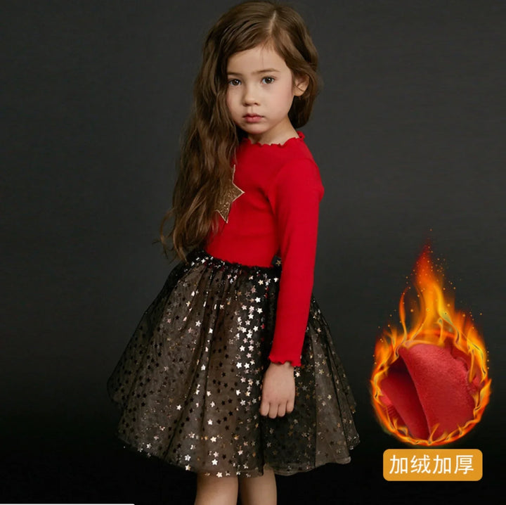 Young girl wearing red long-sleeve top with gold star and black star-patterned skirt on dark background
