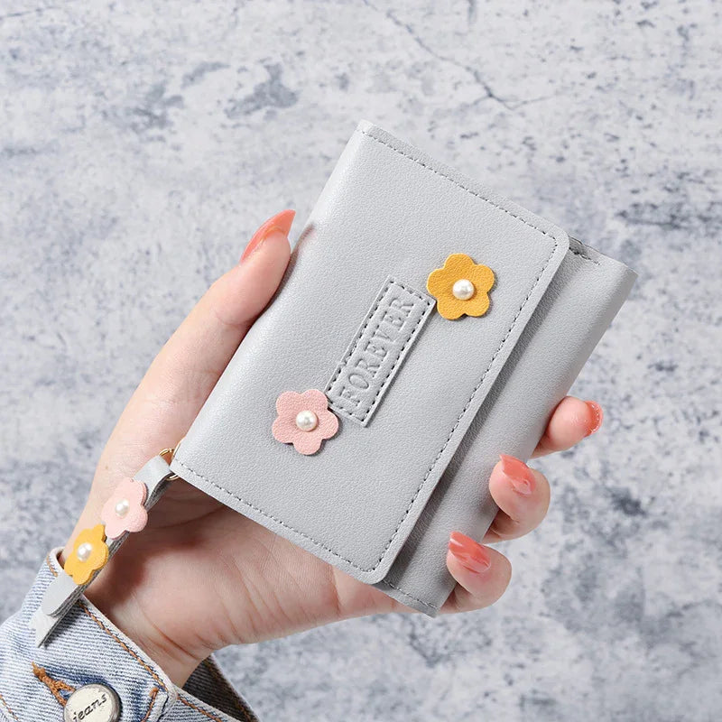 Hand holding a light gray wallet with pink and yellow flower decorations and embossed FOREVER text