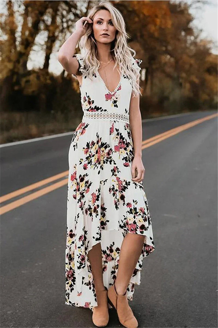 Blonde woman wearing white floral sleeveless high-low dress and tan ankle boots standing on road with autumn trees