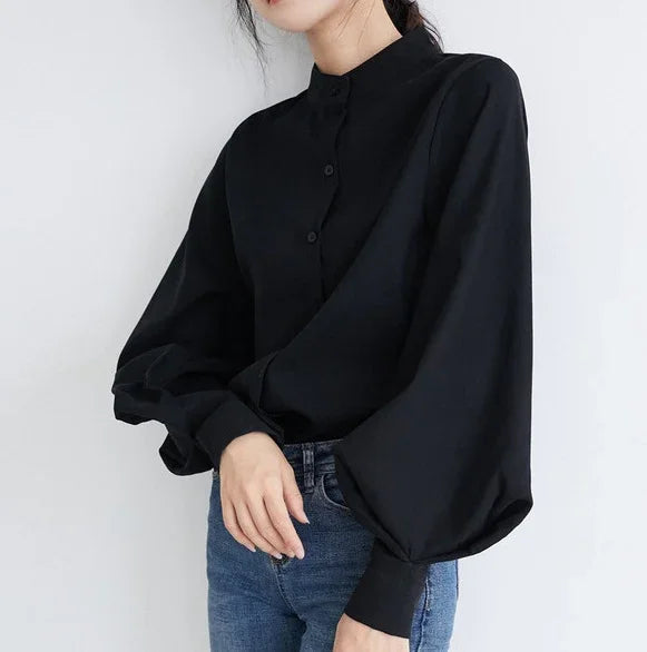 Woman wearing a black bishop sleeve button-up blouse paired with blue jeans on white background