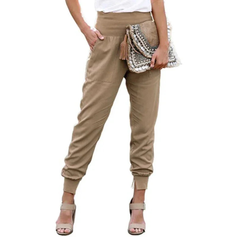 Woman wearing beige high-waist jogger pants and beige high-heeled sandals holding a decorative clutch bag
