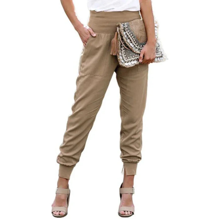 Woman wearing beige high-waist jogger pants and beige high-heeled sandals holding a decorative clutch bag