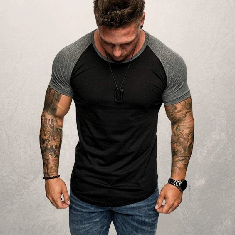muscular man with tattooed arms wearing black and gray raglan t-shirt and jeans against gray background