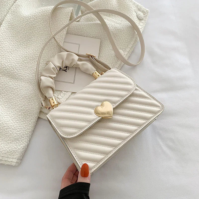 Cream quilted crossbody bag with gold heart clasp and ruched handle on white fabric