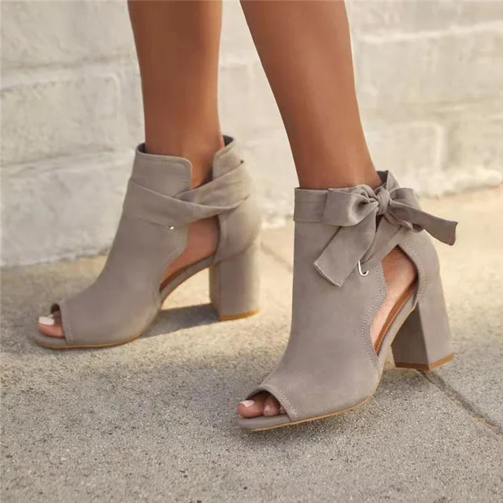 Gray suede peep-toe ankle boots with block heels and bow detail worn on pavement