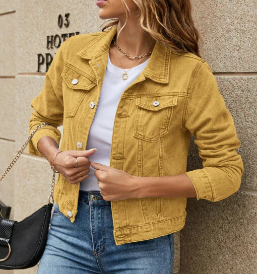 Woman wearing mustard yellow denim jacket over white top with blue jeans, accessorized with necklace and black handbag.