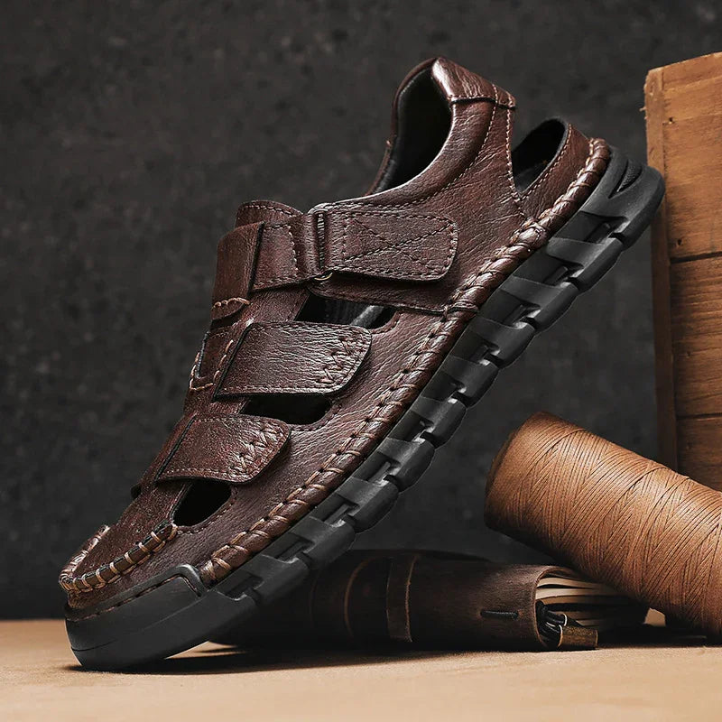Brown leather men's sandal with black sole and stitched details, displayed with leather craft tools
