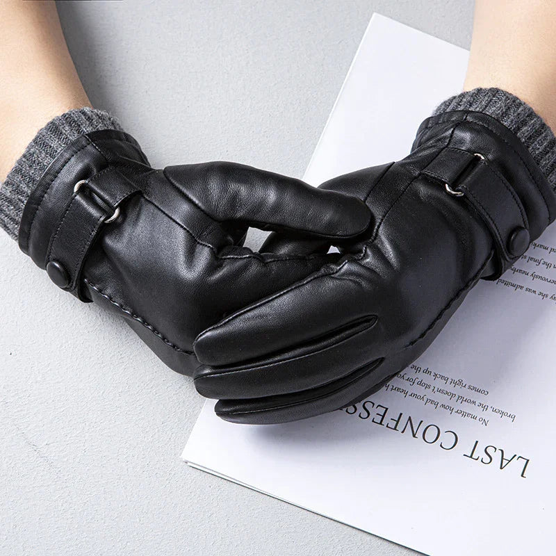 Pair of black leather gloves with gray knit cuffs and buckle strap on a light surface