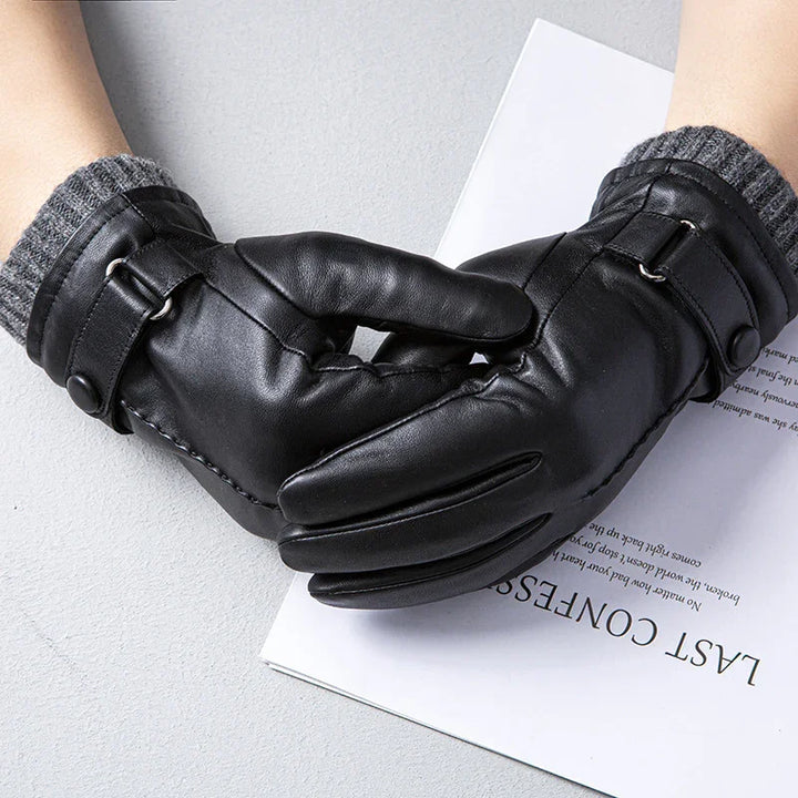 Pair of black leather gloves with gray knit cuffs and buckle strap on a light surface