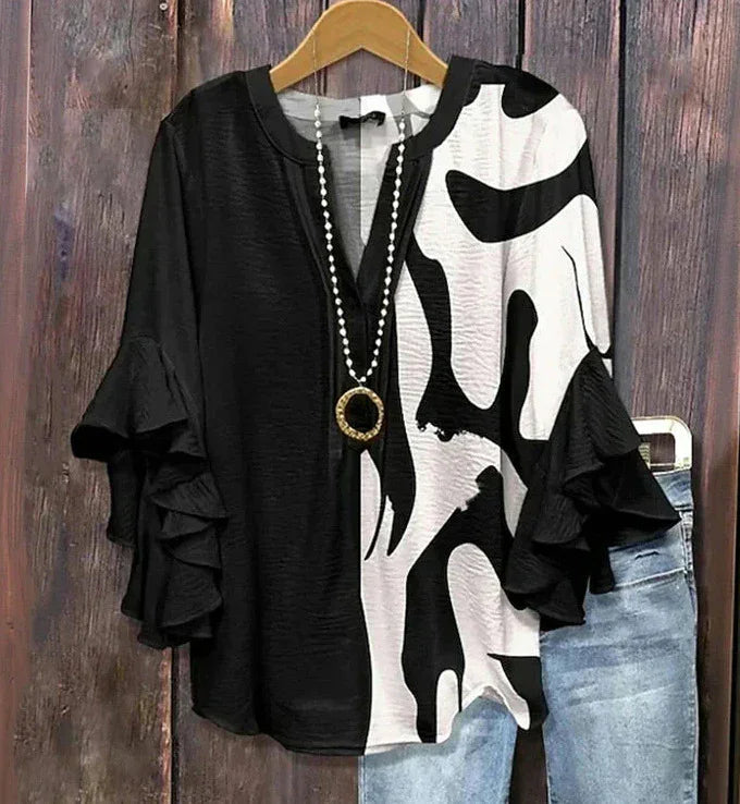 Black and white abstract print blouse with ruffle sleeves on wooden hanger with blue jeans