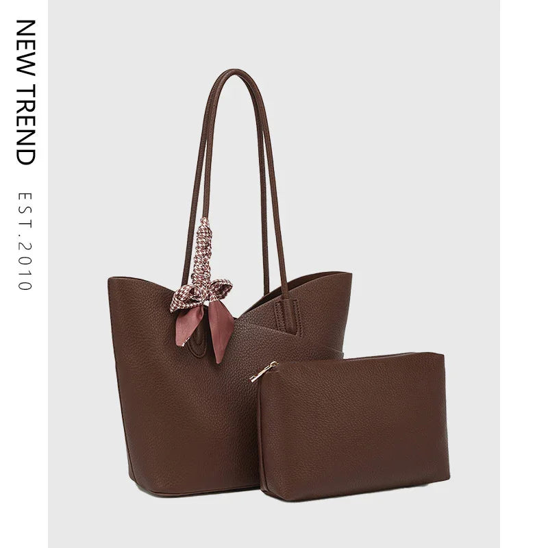 Brown leather tote bag with matching pouch and decorative fabric tied on handle on gray background
