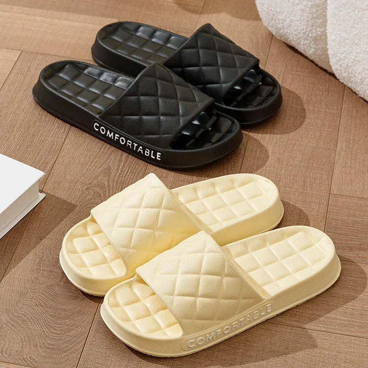 Black and beige quilted slide slippers with cushioned soles on wooden floor, labeled comfortable