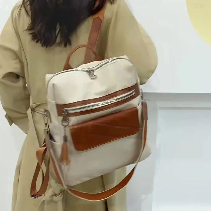 Person wearing beige trench coat with cream and brown leather backpack in indoor setting