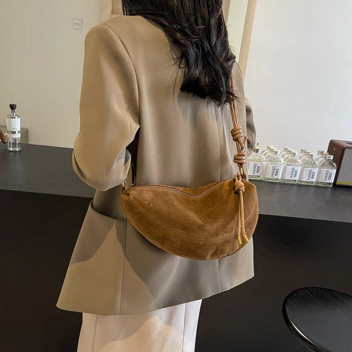 Woman wearing beige blazer carrying a brown suede shoulder bag with knotted strap indoors