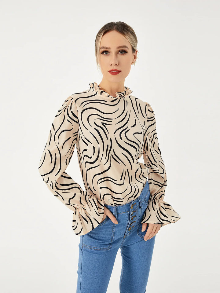 woman wearing beige blouse with black abstract stripes and ruffled cuffs paired with high-waisted blue jeans