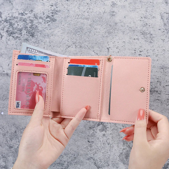 Hands holding open pink leather wallet with credit cards and cash on gray textured background